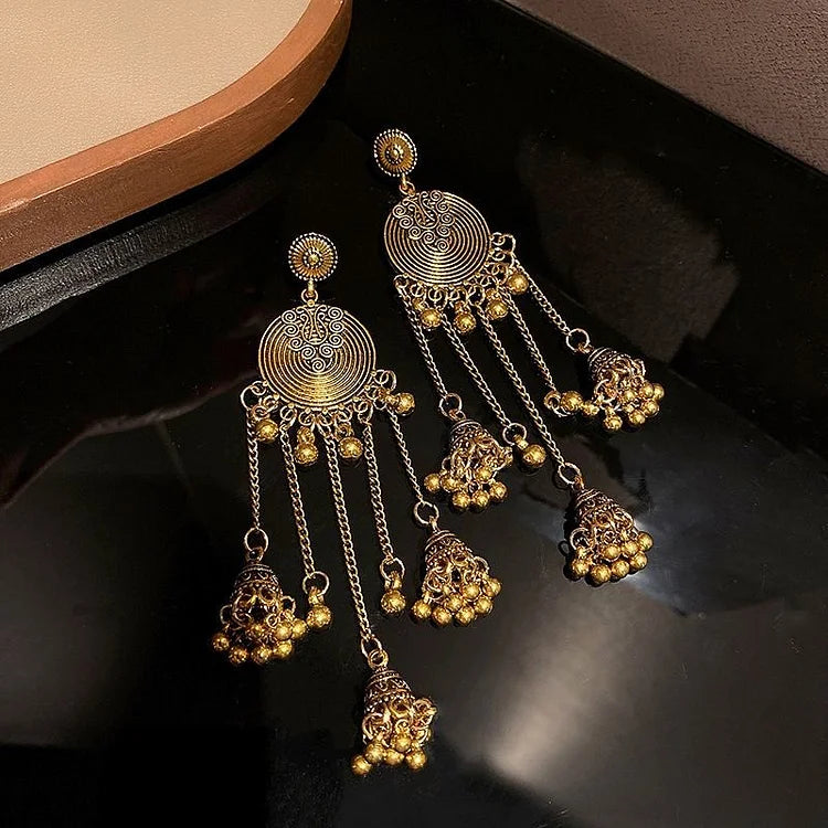 Goldene, orientalische Ohrringe mit filigranen Mustern und hängenden Perlen auf schwarzem Hintergrund.