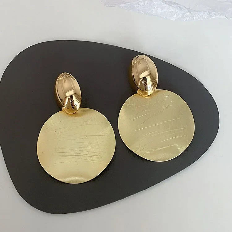 Goldene, runde Ohrringe aus Metall auf schwarzem Hintergrund, elegantes Schmuckdesign.