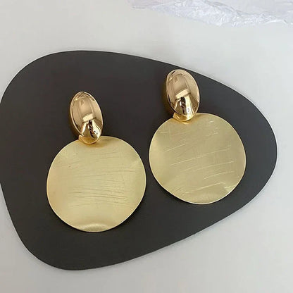 Goldene, runde Ohrringe aus Metall auf schwarzem Hintergrund, elegantes Schmuckdesign.