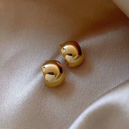 Goldene, glänzende Ohrringe auf beigem Stoff, eleganter Schmuck, modisches Accessoire.