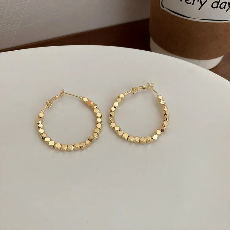 Goldene Creolen Ohrringe auf weißem Teller, geometrisches Design, modischer Schmuck.