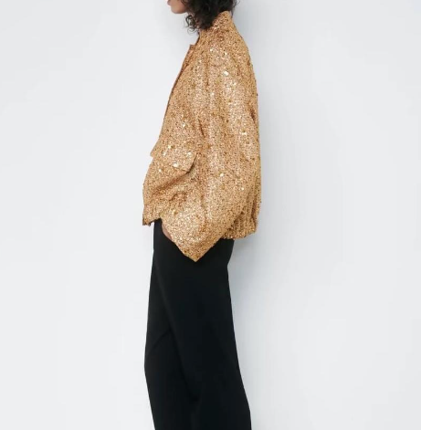 Frau in goldener Paillettenjacke und schwarzer Hose, seitlich, modisch, elegant.