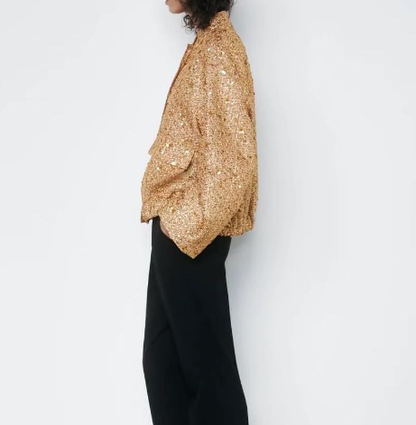 Frau in goldener Paillettenjacke und schwarzer Hose, seitlich, modisch, elegant.