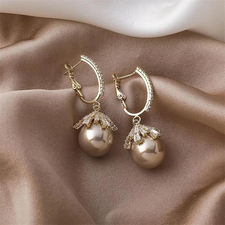 Goldene Ohrringe mit Perlen und Kristallen auf Seidenstoff, eleganter Schmuck für Damen.