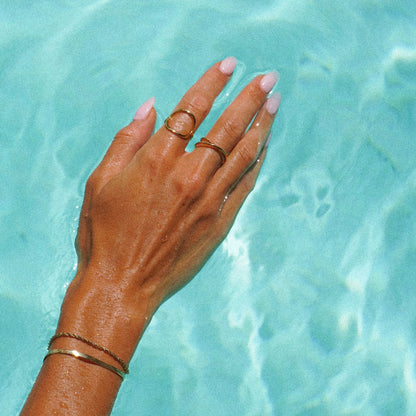 Hand mit goldenen wasserdichten Ringen im Pool, Schmuck, Sommer, stilvoll, elegant.