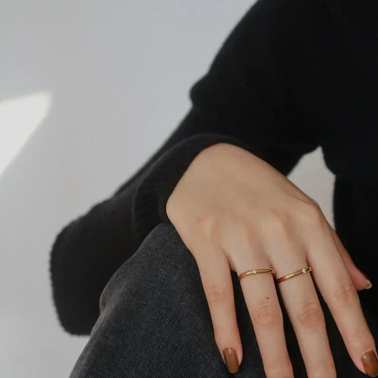 Hand mit zwei goldenen Ringen, schwarzer Pullover, minimalistisch, Schmuck, Modeaccessoire.