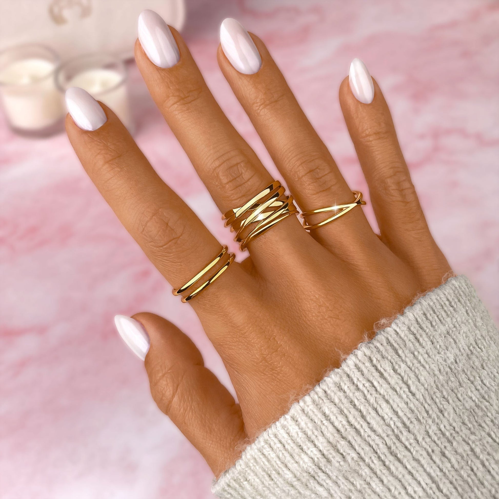 Damenhand mit goldenen Ringen, weiß lackierte Nägel, rosa Hintergrund, Modeaccessoires.