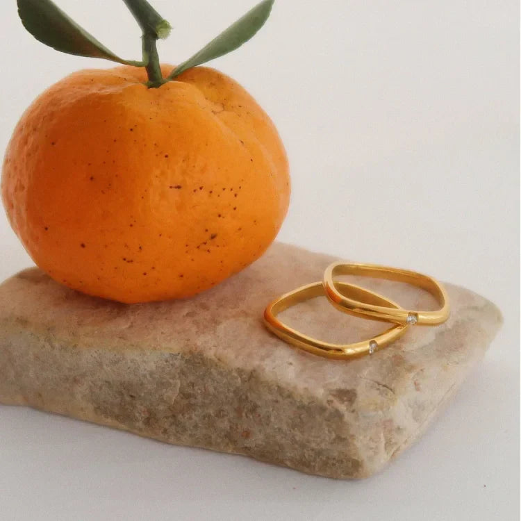Goldene Ringe mit Diamanten auf Stein neben Mandarine, Schmuck, minimalistisch, elegant.