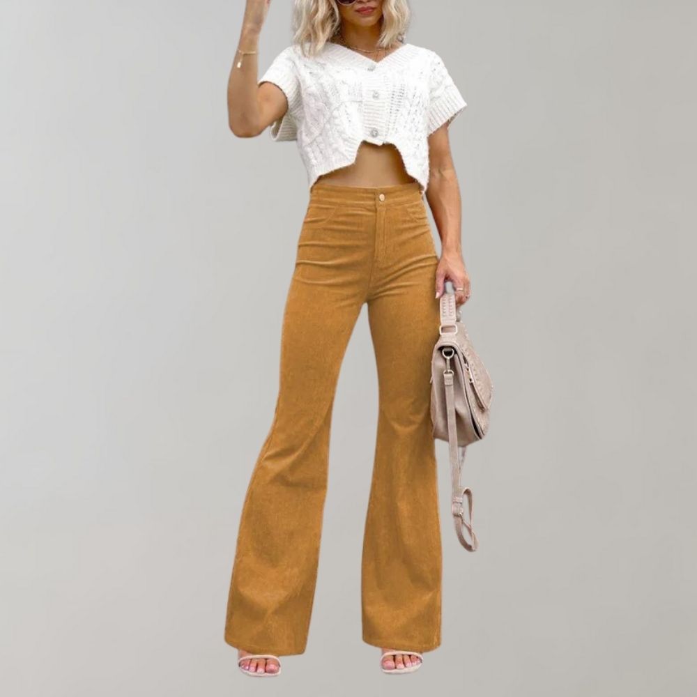 Frau in weißem Crop-Top und goldener Schlaghose, hält beige Handtasche.