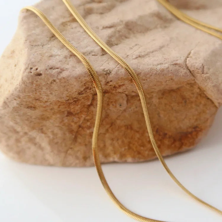 Goldene Schlangenkette auf Stein, elegantes Schmuckdesign, modisches Accessoire für Damen.