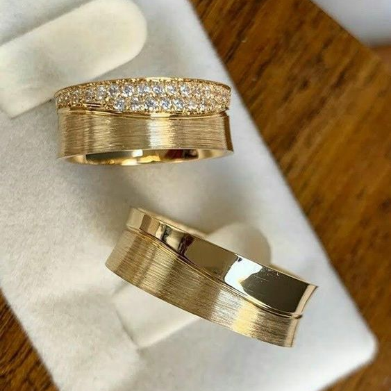 Zwei goldene Eheringe, einer mit Diamanten, auf weißem Hintergrund.