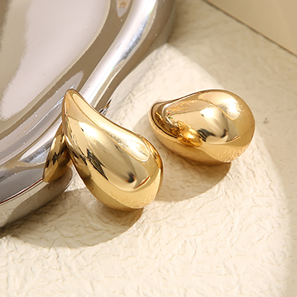 Goldene, tropfenförmige Ohrringe aus Metall auf beigem Hintergrund, glänzend und elegant.