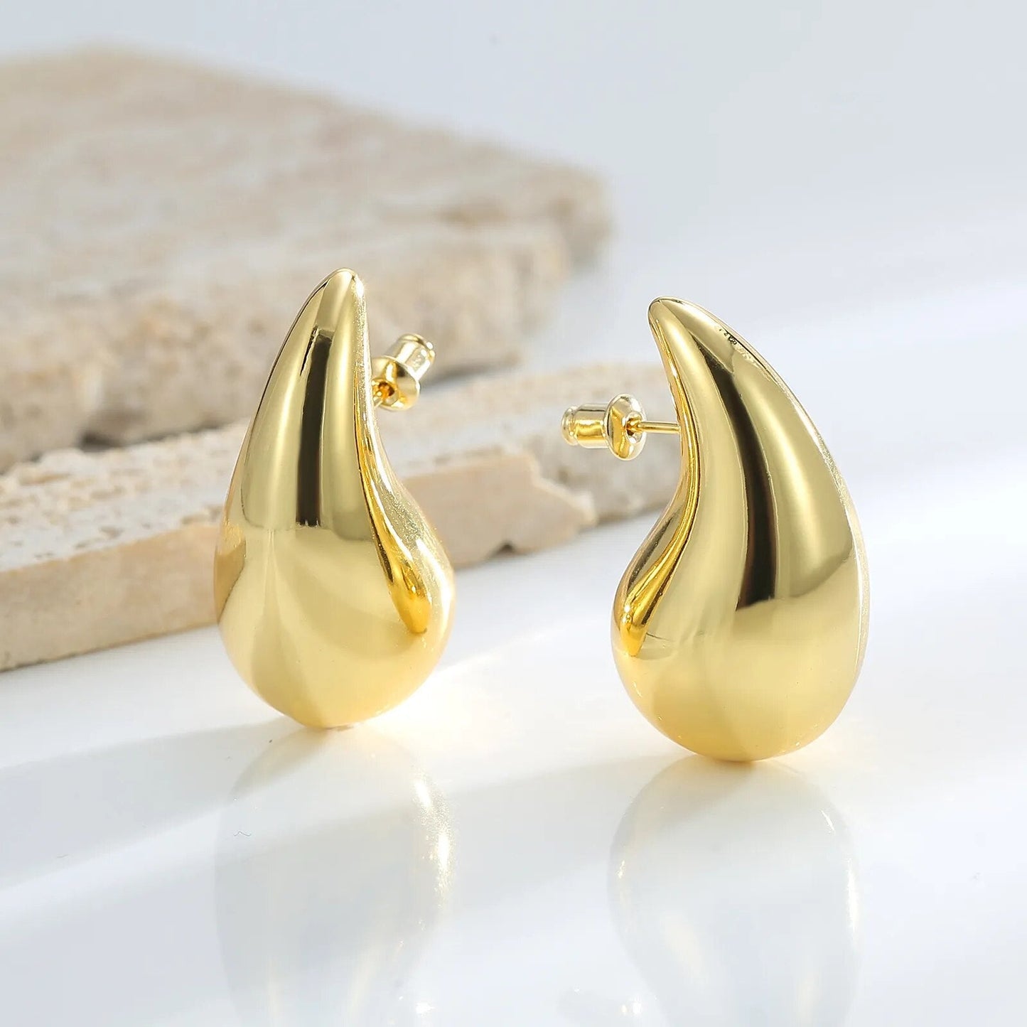 Goldene Tropfen-Ohrringe aus Edelstahl, glänzend, modisch, auf weißem Hintergrund.