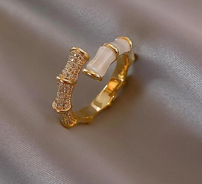 Goldener Ring mit Bambus-Design, Zirkonia-Steinen und Perlmutt auf Seidenstoff.