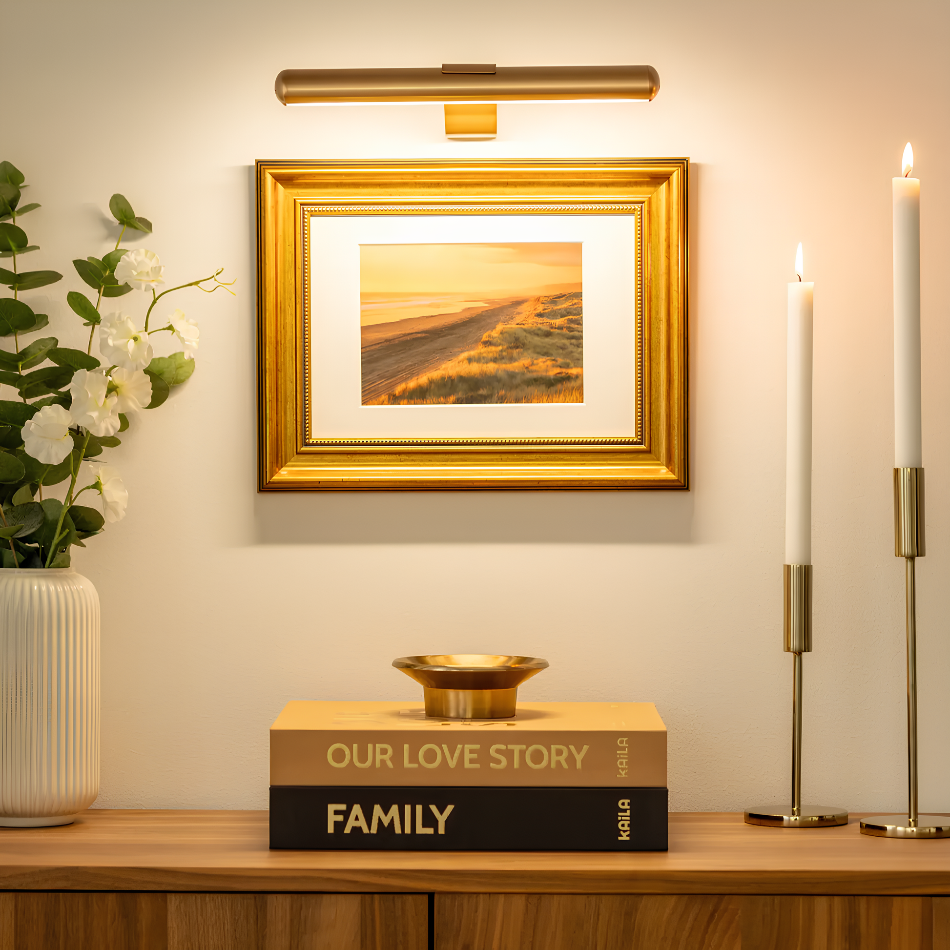Goldener Bilderrahmen mit Landschaftsfoto, umgeben von Kerzen und Büchern auf Holzkommode.