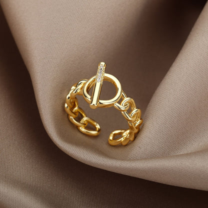 Goldener Ring mit Kettendesign und Zirkonia, modisches Schmuckstück auf beigem Stoff.