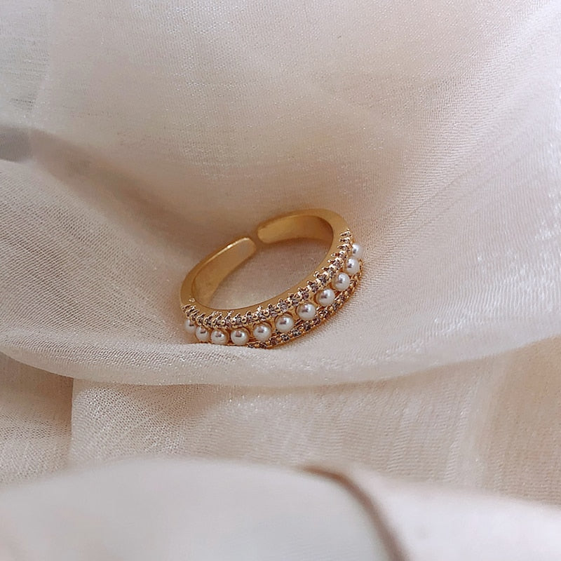Goldener verstellbarer Ring mit Perlen und Strasssteinen auf beigem Stoff.