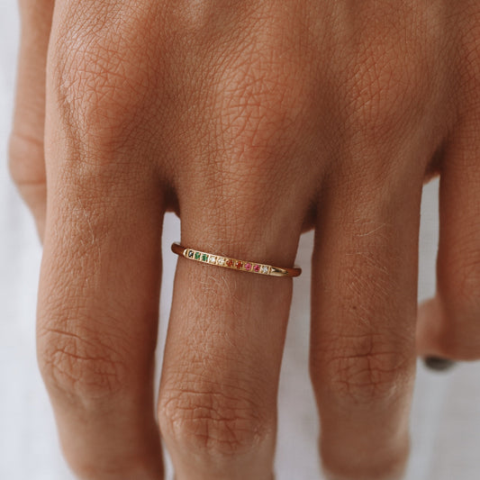 Goldener Regenbogenring mit bunten Edelsteinen auf Hand getragen.