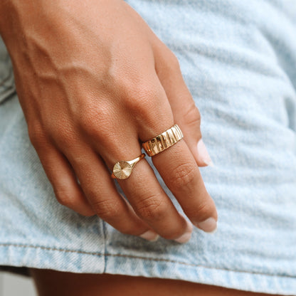 Goldene Ringe an Hand, einer mit Rillenmuster, auf Jeanshintergrund.