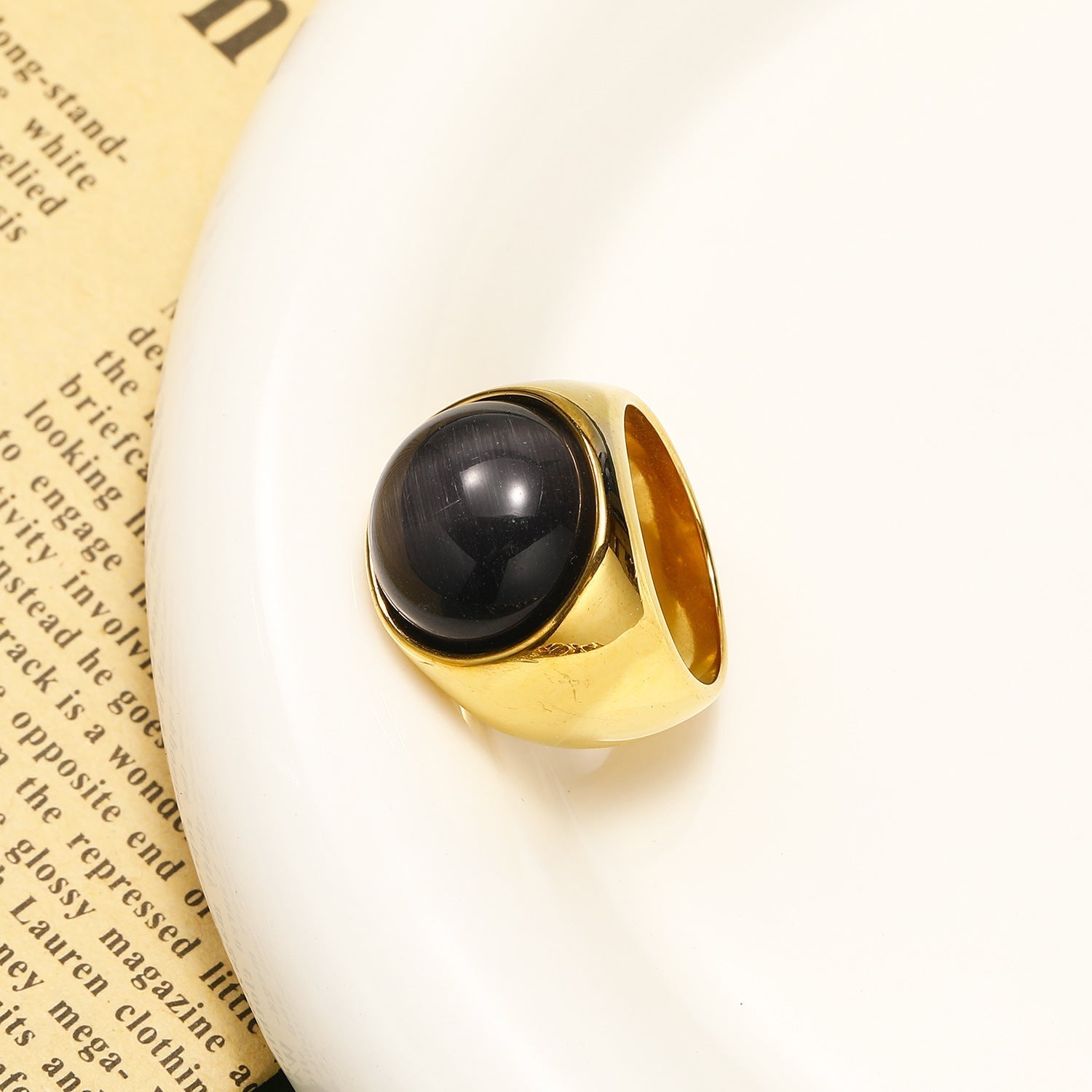 Goldener Ring mit schwarzem Stein auf weißem Teller, elegantes Schmuckdesign.