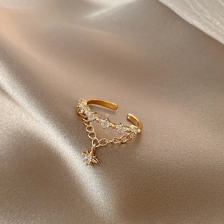 Goldener verstellbarer Ring mit Zirkonia und Sternanhänger auf beigem Satin.