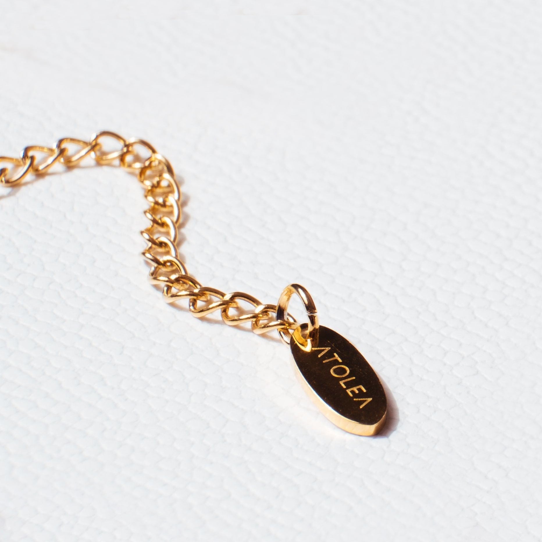 Goldenes Armband mit ATOLEA-Anhänger auf weißem Hintergrund, Schmuck, Modeaccessoire.
