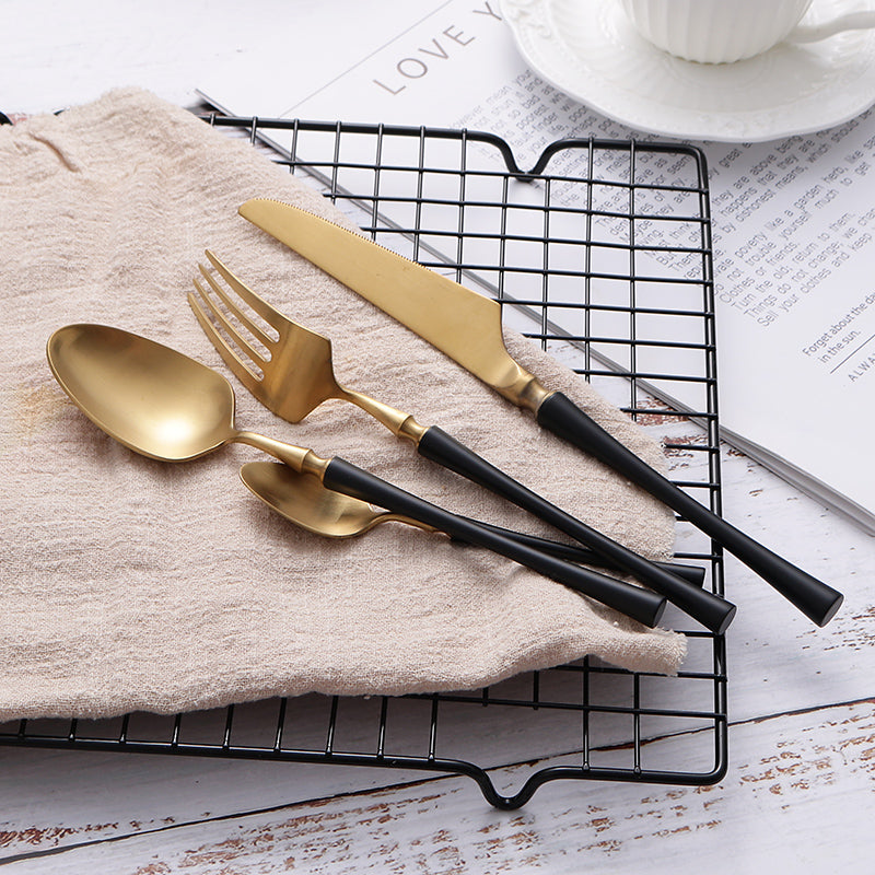 Goldenes Besteckset mit schwarzem Griff auf Handtuch, bestehend aus Messer, Gabel, Löffel.