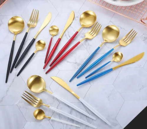Goldenes Besteckset mit bunten Griffen, Gabeln, Löffeln und Messern auf Marmorhintergrund.