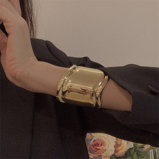 Goldenes, breites Metallarmband mit asymmetrischen Wellenöffnungen, modisch und auffällig.