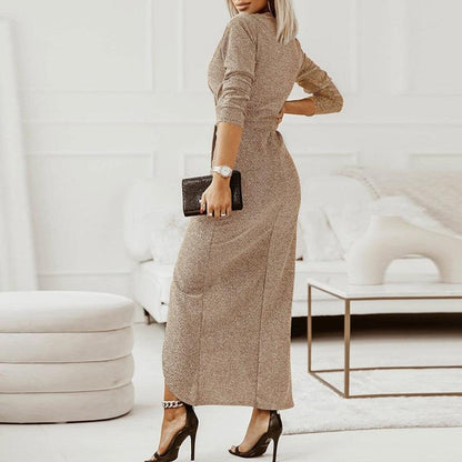 Frau in elegantem, langem, goldfarbenem Kleid mit Clutch und High Heels in modernem Wohnzimmer.