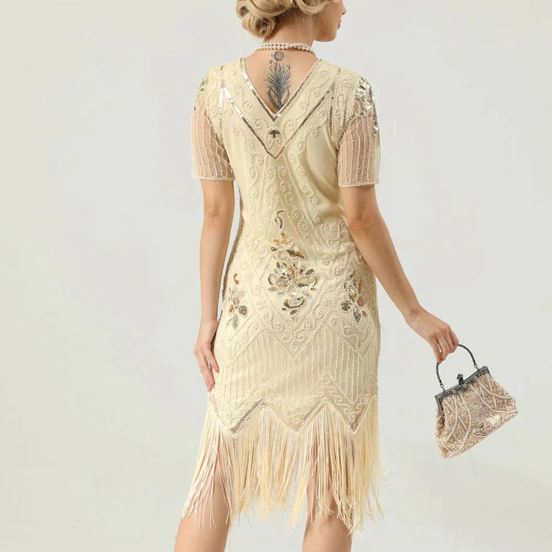 Frau in cremefarbenem Fransen-Kleid mit Pailletten, Vintage-Stil, hält eine kleine Tasche.
