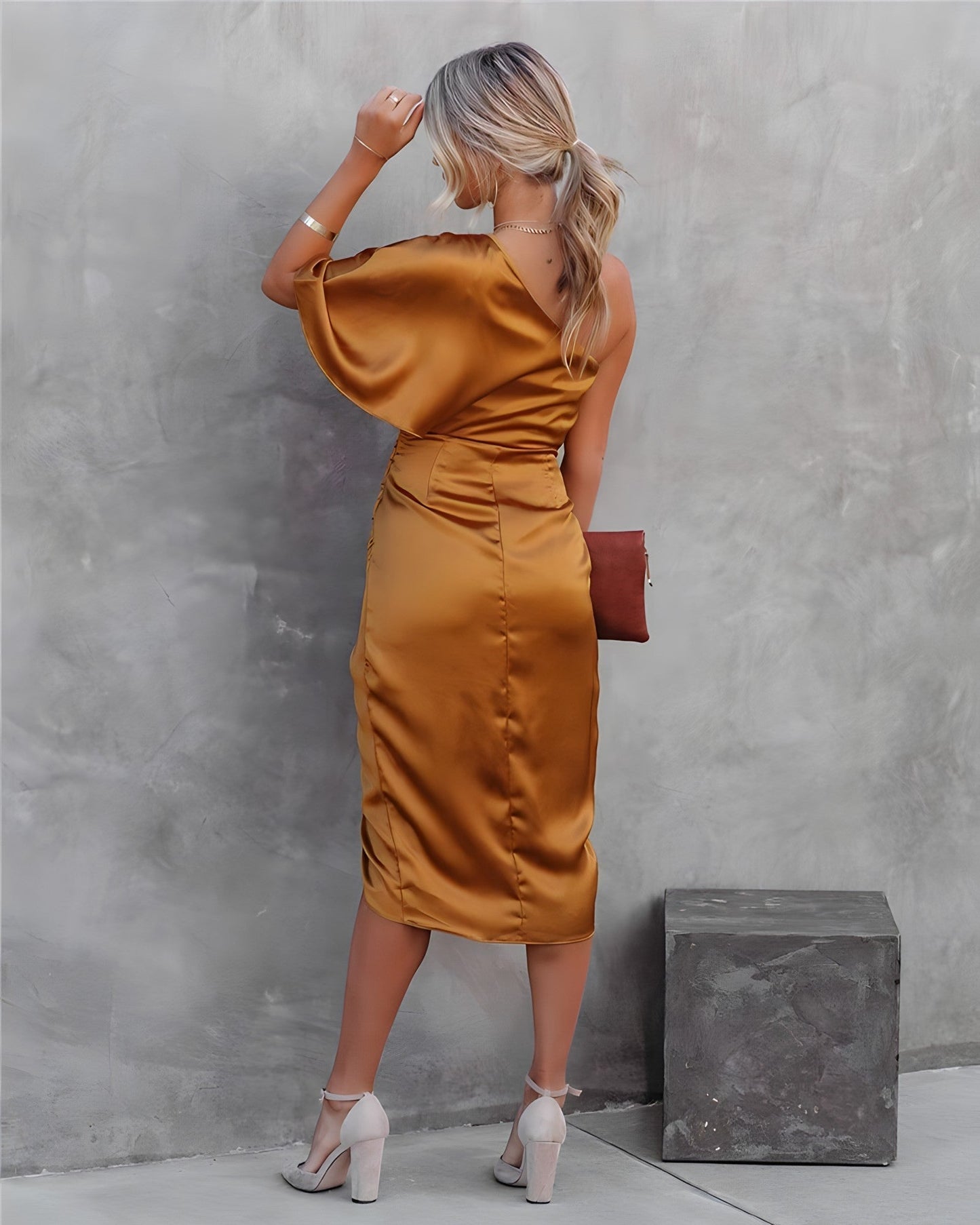 Frau in goldfarbenem Satin-Kleid, schulterfrei, mit Clutch, elegante Abendmode.