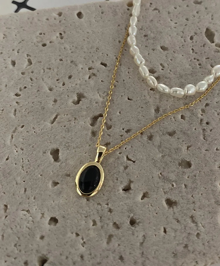 Goldene Halskette mit schwarzem Anhänger auf Stein, elegante Schmuckkette, Damenaccessoire.