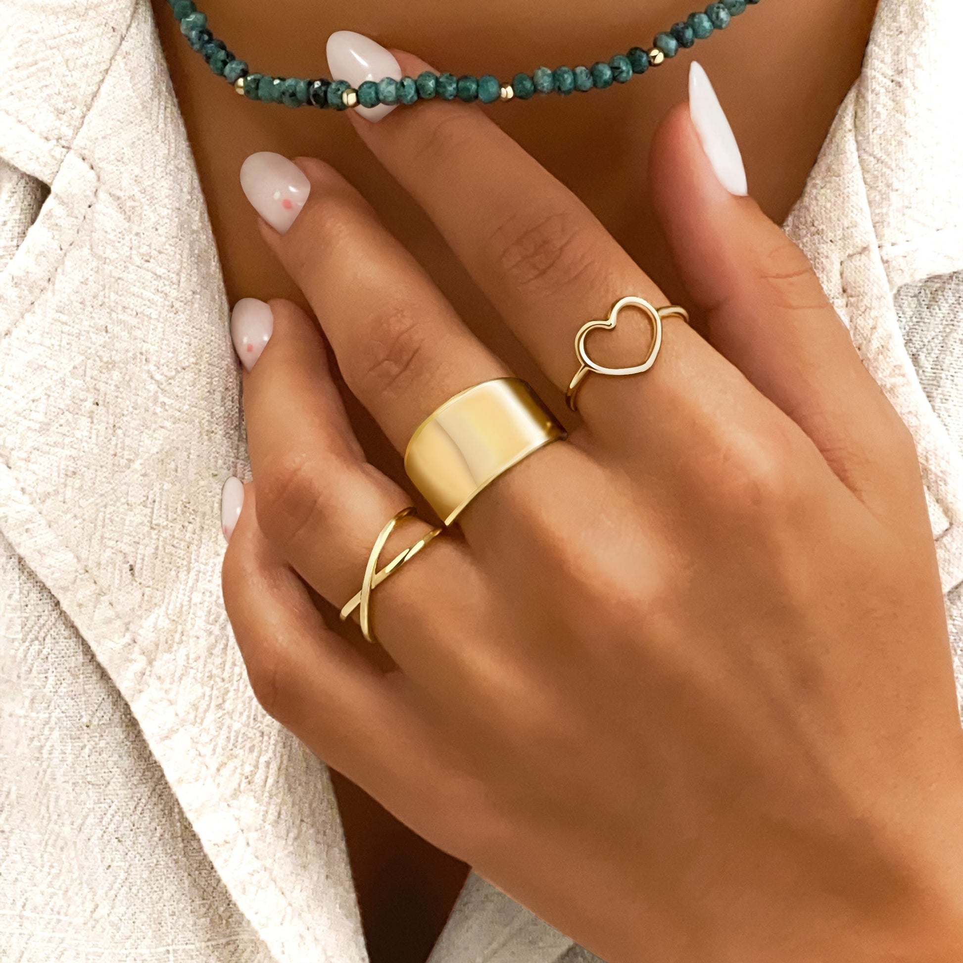 Damenhand mit goldenen Ringen und türkisfarbener Halskette, eleganter Schmuck, Nahaufnahme.