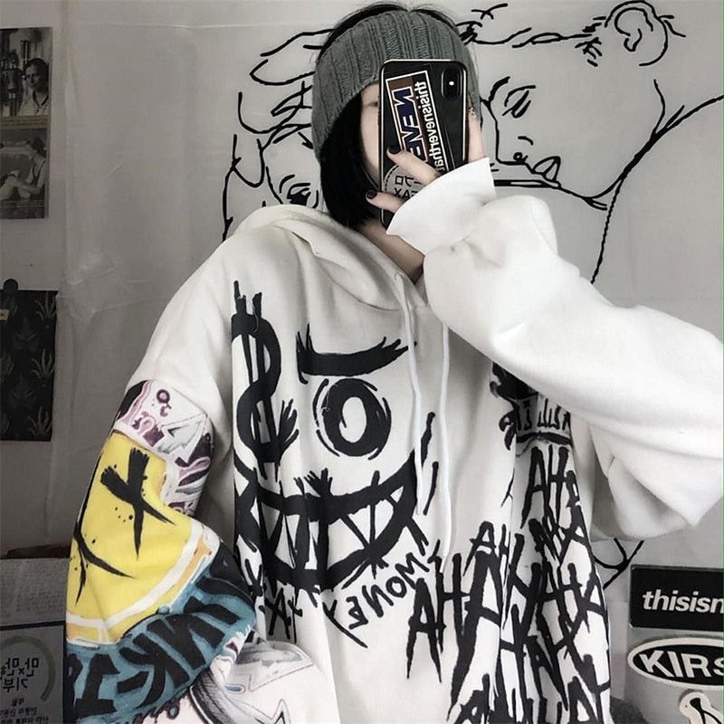 Person in weißem Graffiti-Hoodie mit Smartphone, grauer Mütze, urbaner Streetwear-Look.
