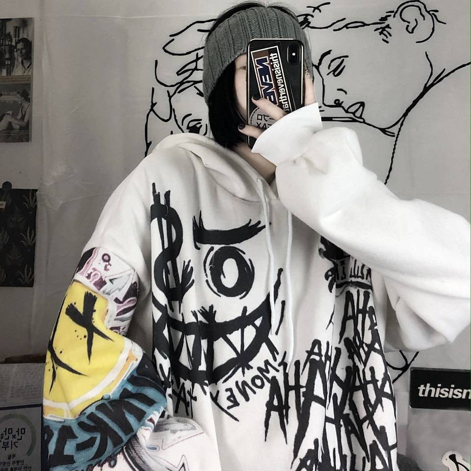 Person in weißem Graffiti-Hoodie mit Smartphone, graue Mütze, urbaner Streetwear-Stil.