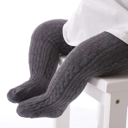 Graue Baby-Strumpfhose aus Baumwolle mit Zopfmuster auf weißem Stuhl.