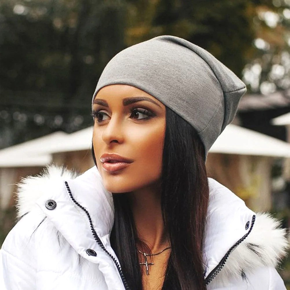 Frau mit grauer Beanie-Mütze und weißer Winterjacke, stilvolle Herbstmode im Freien.
