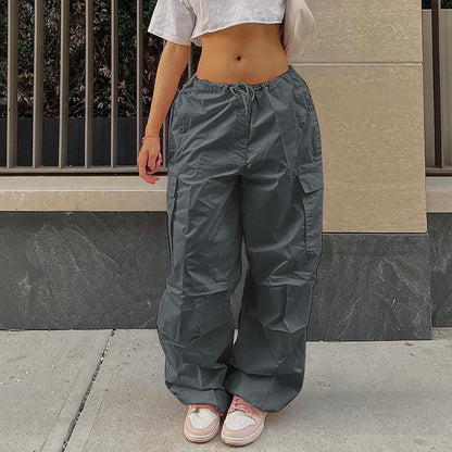 Frau in grauer Cargohose, weißem Crop-Top, rosa Sneakers, urbaner Hintergrund.