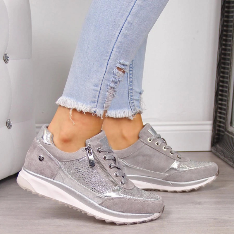 Graue Damen-Sneaker mit Reißverschluss, silbernen Details, bequem, modisch, auf Holzboden.