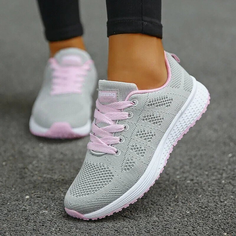 Graue Damen-Laufschuhe mit rosa Schnürsenkeln, atmungsaktiv, sportlich, auf Asphalt.