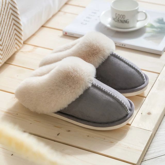 Graue Hausschuhe mit weißem Fellfutter auf Holzfußboden, gemütliche Winterpantoffeln.