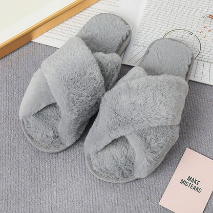 Graue flauschige Hausschuhe, überkreuztes Design, weiches Material, auf Teppichboden.