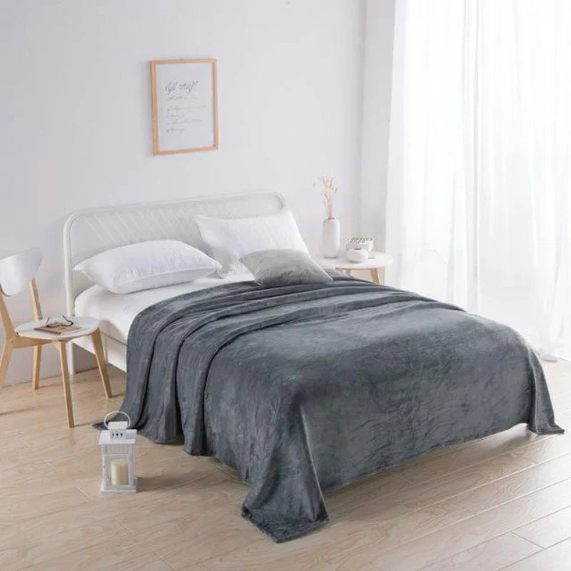 Graue Kuscheldecke auf weißem Bett in modernem Schlafzimmer, gemütliche Wohnkultur, Tageslicht.