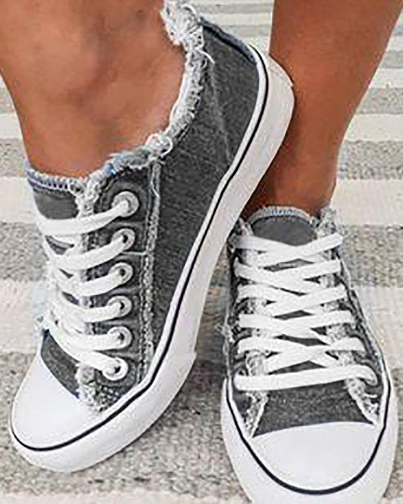 Graue Damen-Sneaker mit weißen Schnürsenkeln, Fransen-Design, auf gestreiftem Teppich.