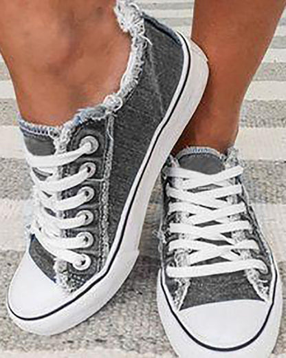Graue Damen-Sneaker mit weißen Schnürsenkeln, Fransen-Design, auf gestreiftem Teppich.