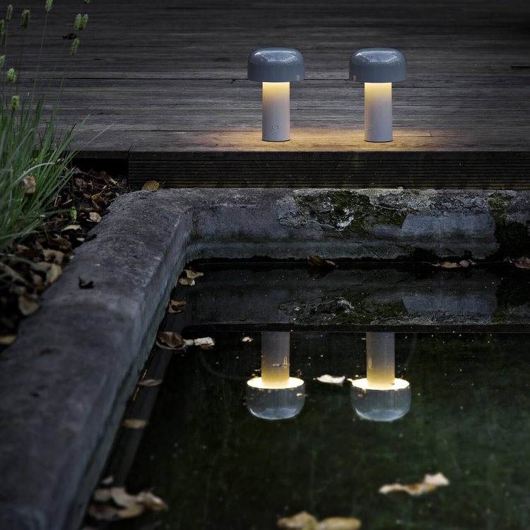 Zwei graue LED-Tischlampen im Freien, reflektiert in einem Teich, stimmungsvolle Beleuchtung.