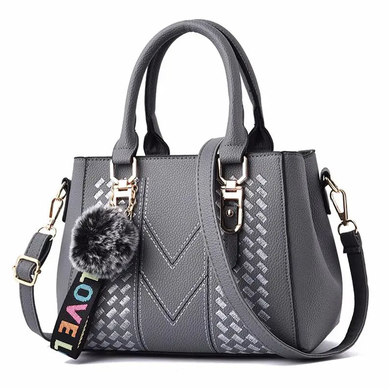 Graue Damenhandtasche mit Schulterriemen, Kunstleder, Pompon-Anhänger, modisches Design.