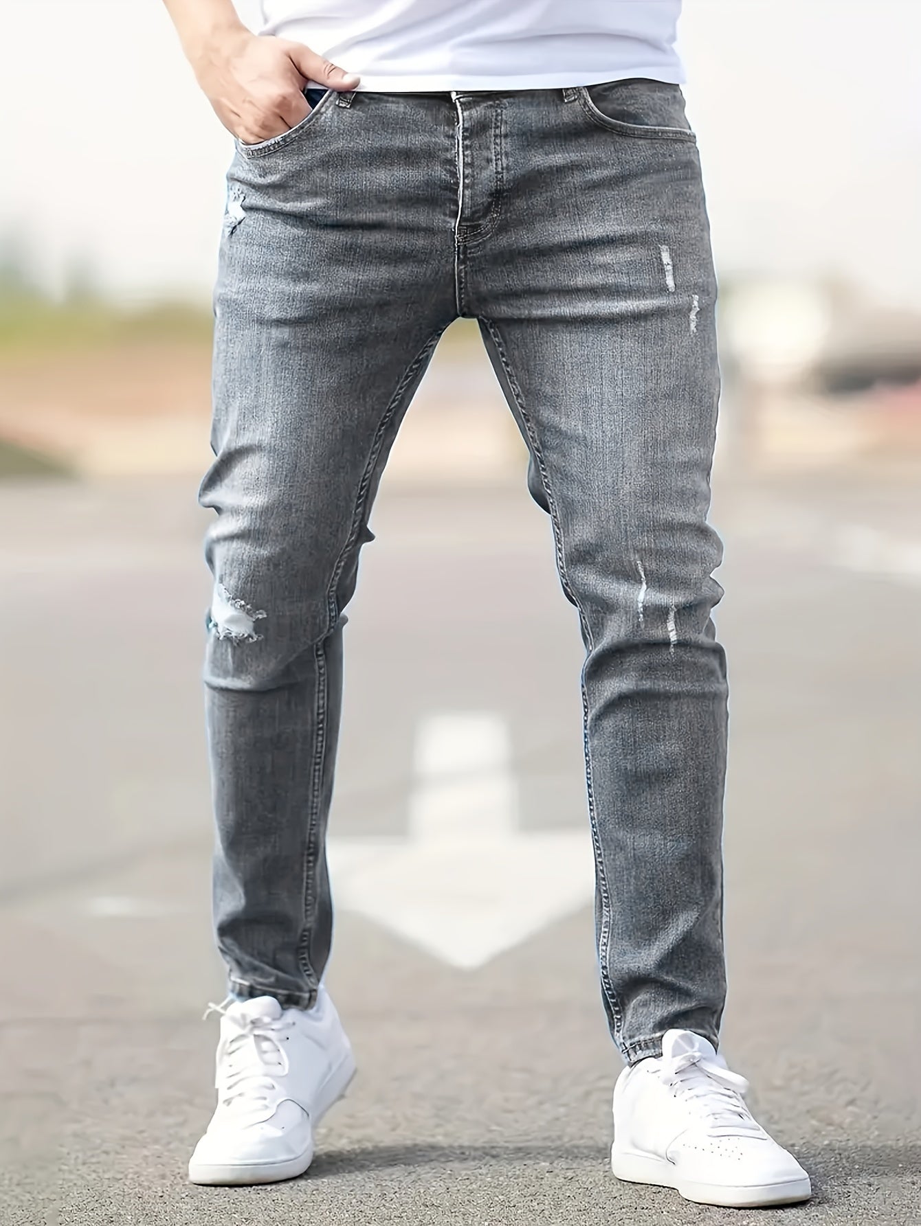 Graue Herren-Jeans, Slim Fit, mit leichten Rissen, getragen mit weißen Sneakern auf Straße.
