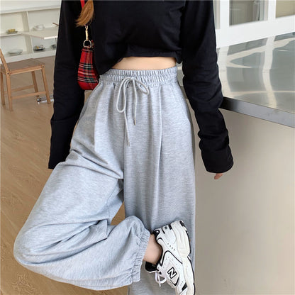 Frau in grauer Jogginghose, schwarzem Langarmshirt, weiße Sneaker, modisch, bequem, Freizeitkleidung.